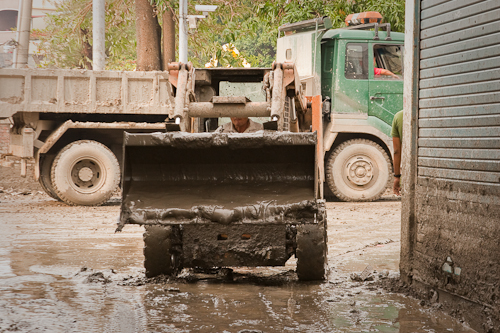 In many back streets clearing the mud by spade allows the smaller machines in.  Mud from within houses and yards can then be broken up, and tossed into the road for them to pick up and transport to... 